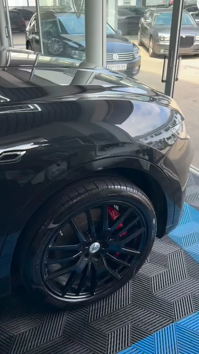 Gereinigte schwarze Felge und Flanke eines SUV auf dem blau-grauen Hallenboden